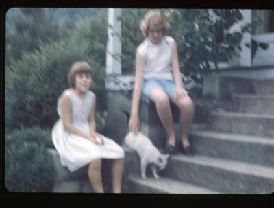 Two girls with a cat sitting on the front steps of a house