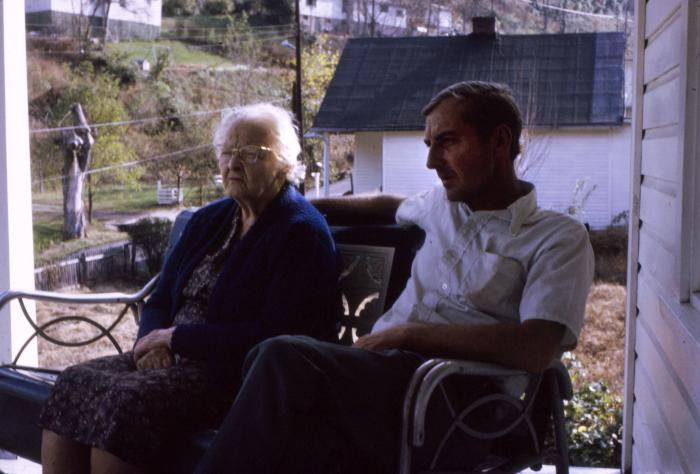 Man and woman sitting on a bench on the porch of a white house