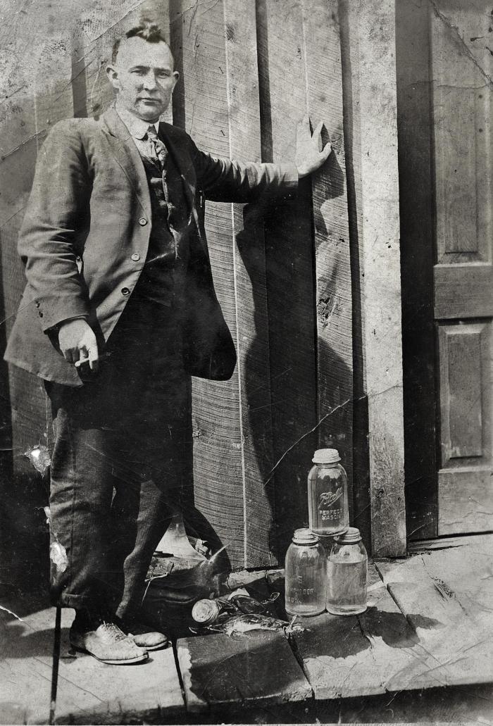 Man standing outside building with moonshine at his feet