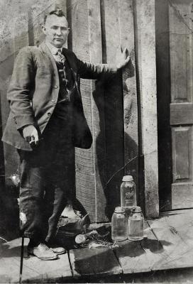 Man standing outside building with moonshine at his feet