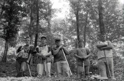 Young men posing with shovels in forest setting
