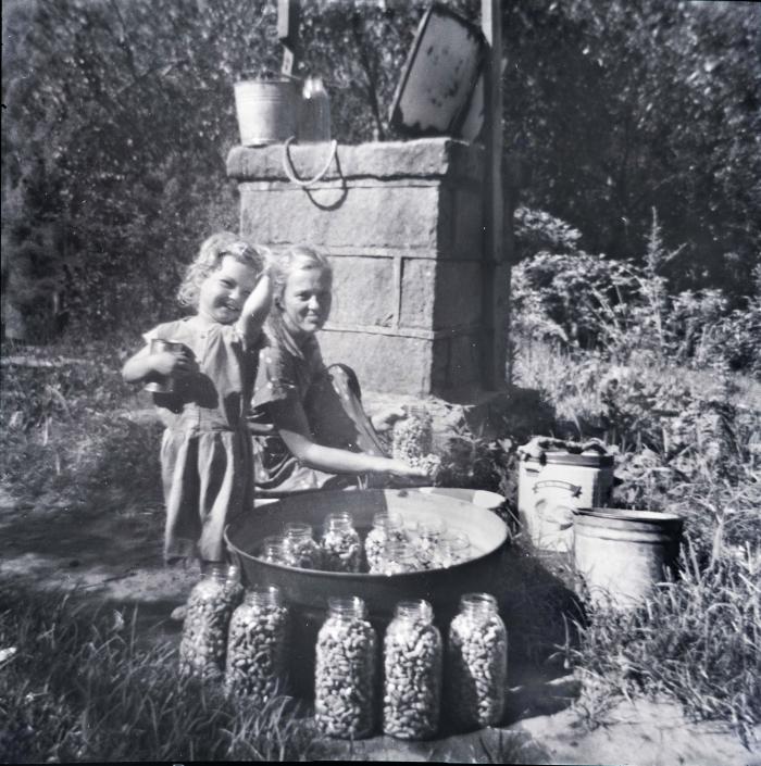 Exterior of woman and daughter canning beans, smiling at camera