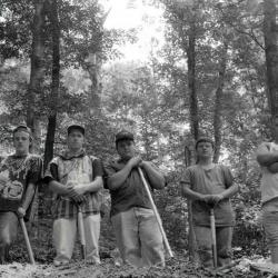 Young men posing with shovels in forest setting