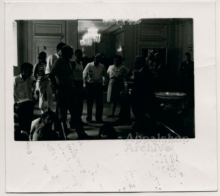 A group of people standing in a room with chandeliers, talking - The Struggle of Coon Branch Mountain