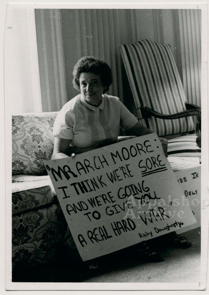 Production still of woman holding protest sign - The Struggle of Coon Branch Mountain