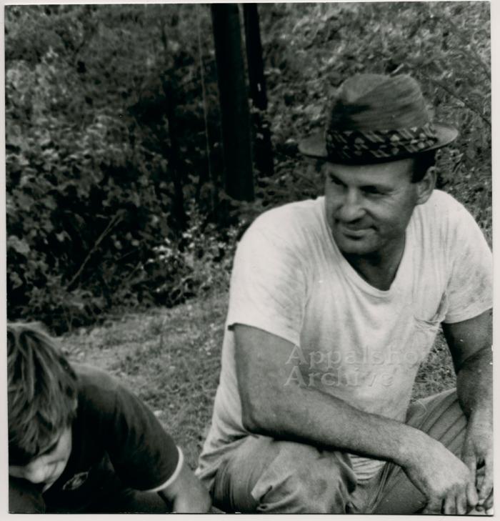 Production still of a man seated next to a young man, exterior - The Struggle of Coon Branch Mountain 