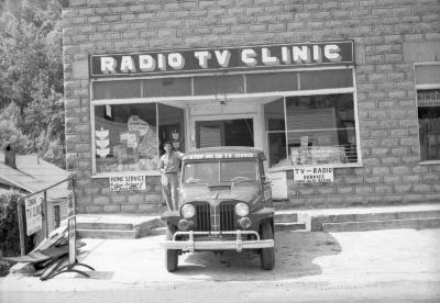 Man posing with car in front of Radio TV Clinic in East Jenkins