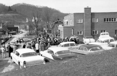 Townspeople in formal attire gathered in lot next to brick building