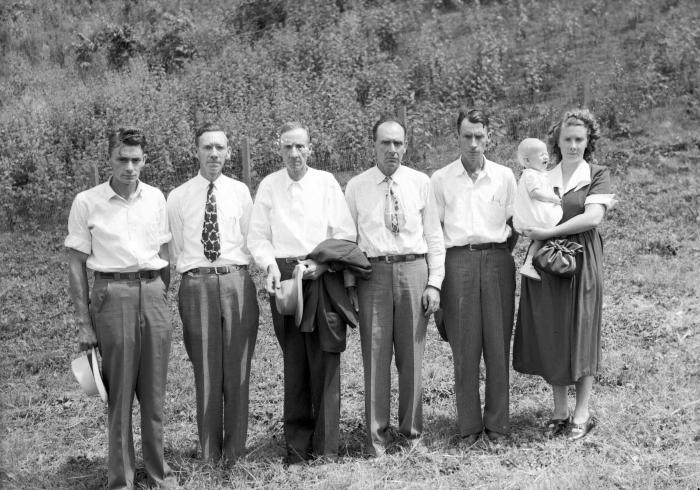 Group portrait of five men, one woman, and crying baby 