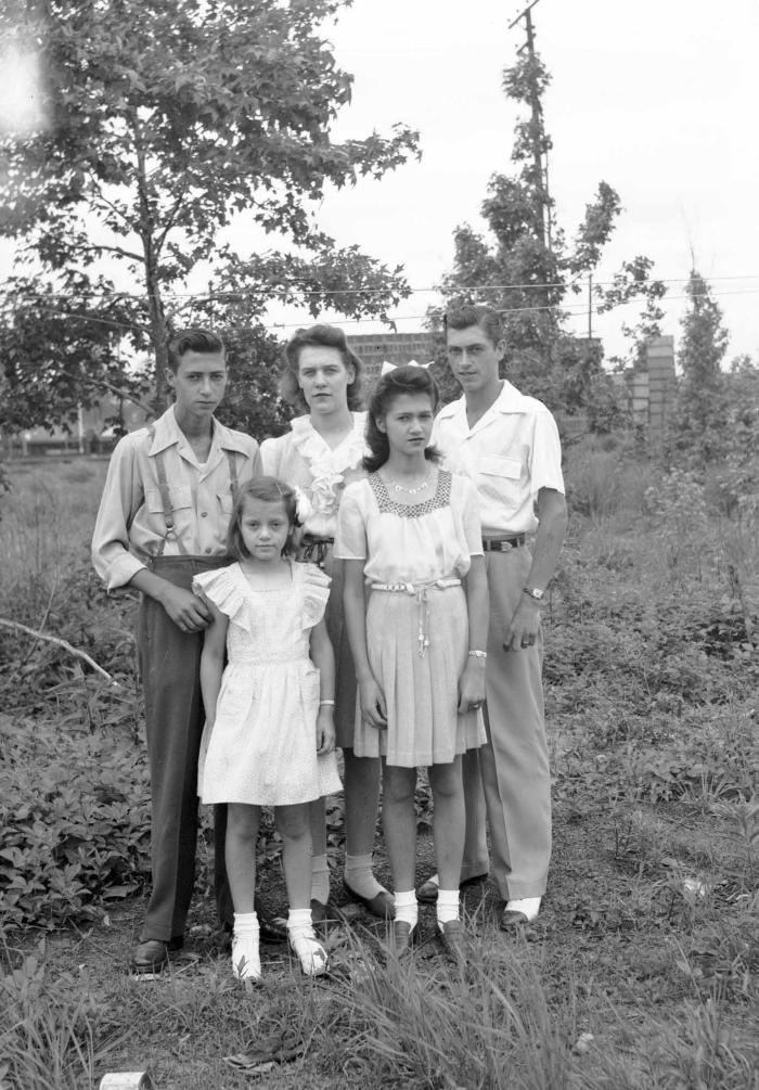 Family of five with styled hair poses amidst foliage