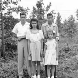 Four youth with styled hair pose amidst foliage