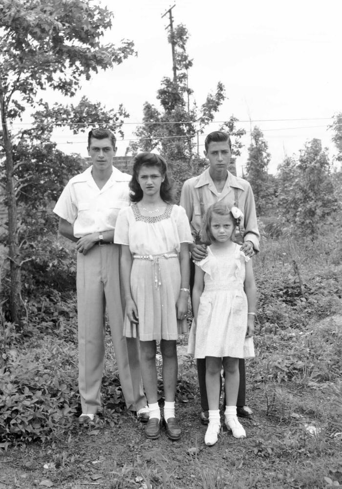 Four youth with styled hair pose amidst foliage