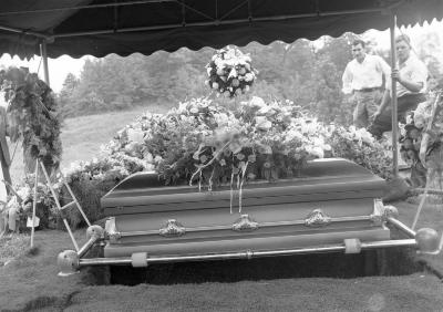 Casket suspended above burial plot adorned with flowers