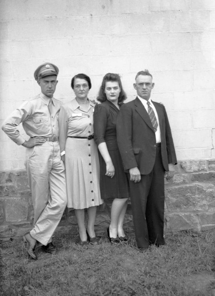 Family of four, one in military uniform, poses in front of brick wall