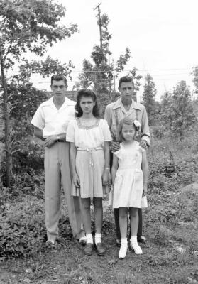 Four youth with styled hair pose amidst foliage