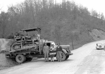 Three men pose in front of truck with "danger" sign