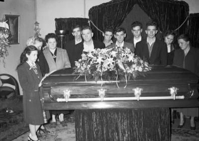 Group portrait in funeral parlor surrounding casket