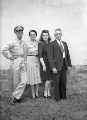 Family of four, one in military uniform, poses in front of brick wall