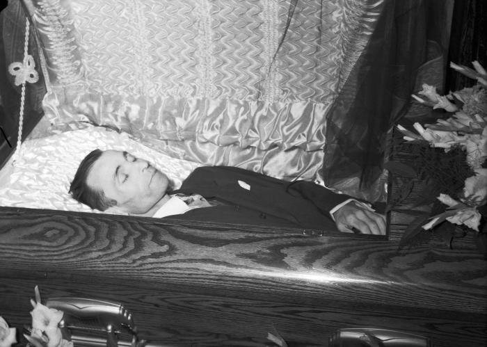 Portrait of man in casket surrounded by gladiolus flowers