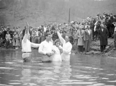Man and woman in white getting baptized in river