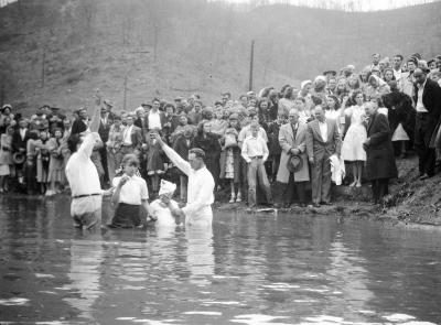 Two children, one in headscarf, getting baptized in river
