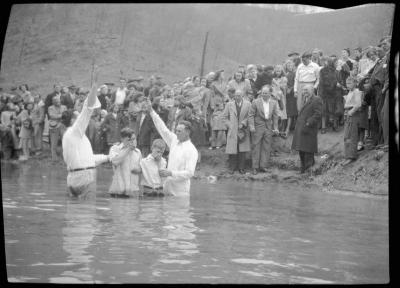 Two boys with mouths covered prepare to get baptized in river