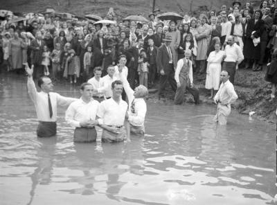 Two young men, one smiling, getting baptized in river