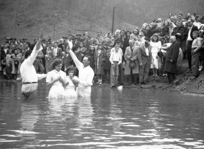 Two children in white dresses getting baptized in river